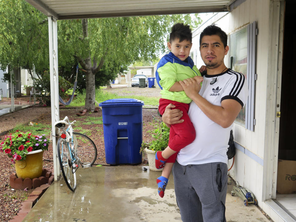 Osvaldo Salas, 29, stands with his son outside their home in suburban Phoenix on Wednesday, March 18, 2020. Salas, who isn't proficient in English, says he's disappointed state authorities haven't posted any information on the coronavirus in Spanish and that he has to rely on friends, family and TV for the latest. Salas, a restaurant cook, is worried about supporting his four children if he can't work anymore. (AP Photo/Astrid Galván)