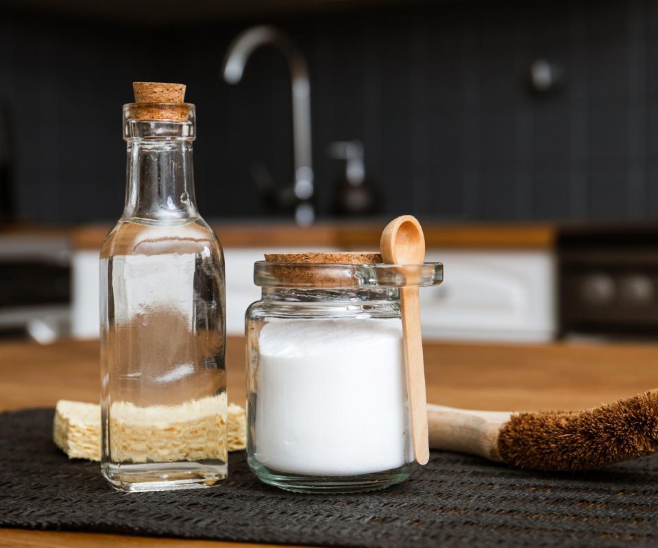 bottle of white vinegar beside a container of sugar and a scrubbing brush