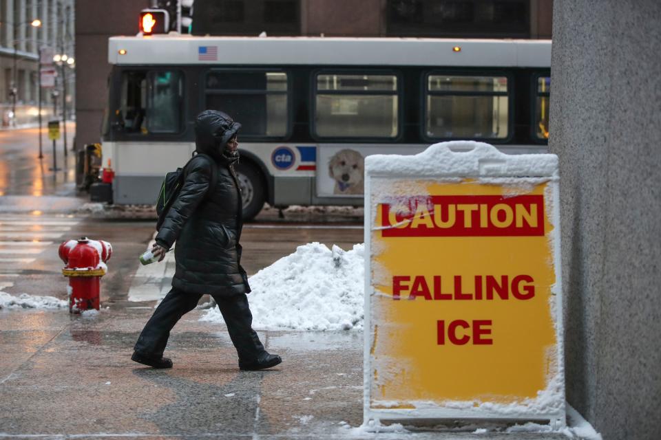 Una mujer camina junto al cartel de Precaución con la caída de hielo en el centro de Chicago, Illinois, el 26 de enero de 2021. - Según el Servicio Meteorológico Nacional, el área podría estar cubierta con 5 a 10 pulgadas de nieve durante la tormenta de nieve más grande en aproximadamente dos años. (Foto de KAMIL KRZACZYNSKI / AFP) (Foto de KAMIL KRZACZYNSKI/AFP a través de Getty Images)