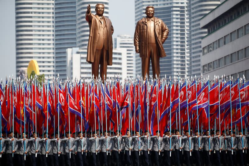 People carry flags in front of statues of North Korea founder Kim Il Sung and late leader Kim Jong Il during a military parade marking the 105th birth anniversary Kim Il Sung in Pyongyang