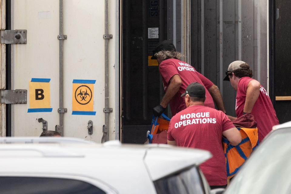 Workers wearing "Morgue Operations" shirts move a body bag into a refrigerated storage container adjacent to the Maui Police Forensic Facility where human remains are stored in the aftermath of the Maui wildfires in Wailuku, Hawaii on August 15, 2023.