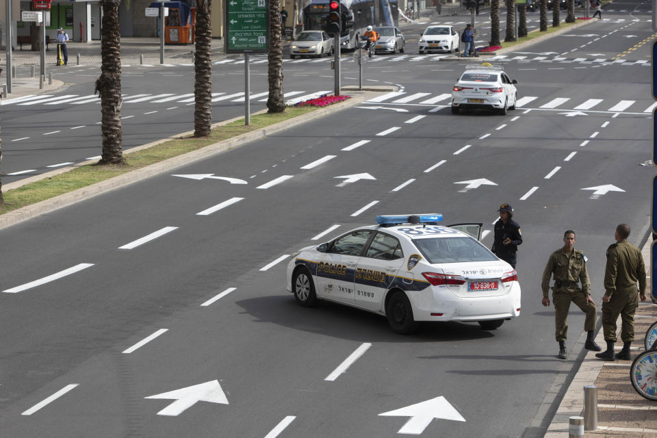 Israeli soldiers stand with police officers at a roadblock near Rabin square in Tel Aviv, Israel, Wednesday, April 1, 2020. Israel's military has deployed hundreds of troops to assist police in enforcing health regulations meant to stem the spread of the new coronavirus. Soldiers and police are setting up roadblocks and inspecting passing cars, asking motorists for their reasons for leaving the house. (AP Photo/Sebastian Scheiner)