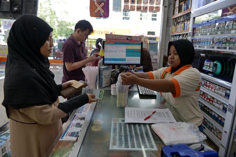 A cashier (R) accepts money from a customer at a supermarket in Kuala Lumpur on April 1, 2015