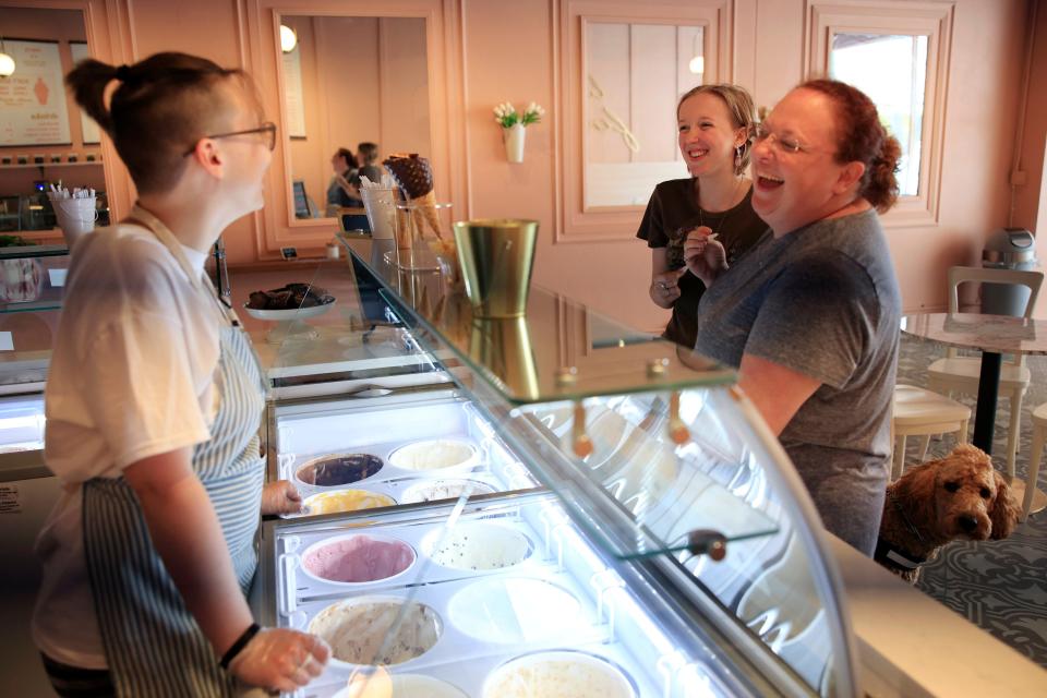 Waffle Cone employee Dawn Bracy (left) talks with  Kaitlyn Michel, 17, and her mother, Ali, as Teddy, a service dog in training peeks for a look at the newly opened Waffle Cone ice cream parlor in Five Points.