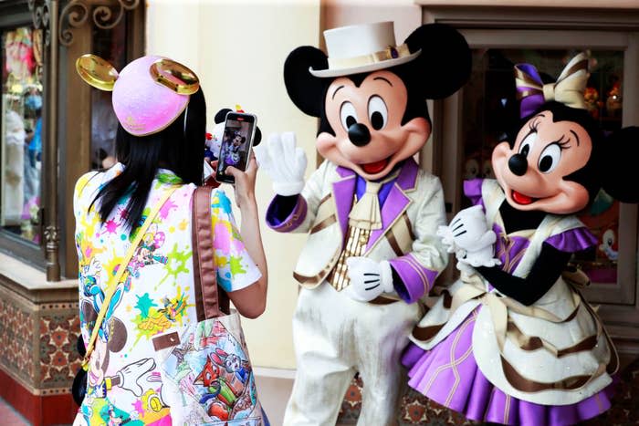 A woman at Disneyland is taking a picture of Mickey and Minnie Mouse