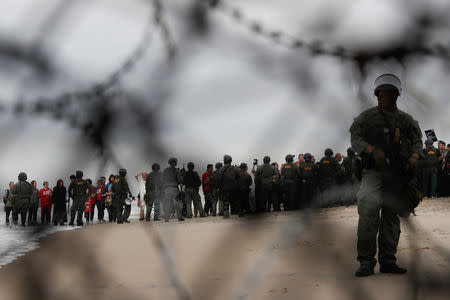 U.S. Customs and Border Protection (CBP) officials stand guard in front of people during a gathering in support of the migrant caravan in San Diego, U.S., close to the border wall between the United States and Mexico, as seen from Tijuana, Mexico December 10, 2018. REUTERS/Carlos Garcia Rawlins