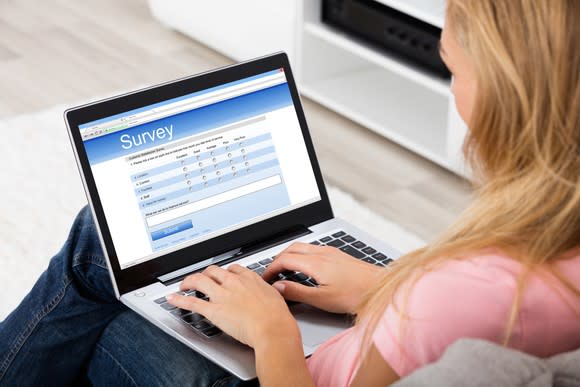 A woman typing on a laptop showing a survey on the monitor.