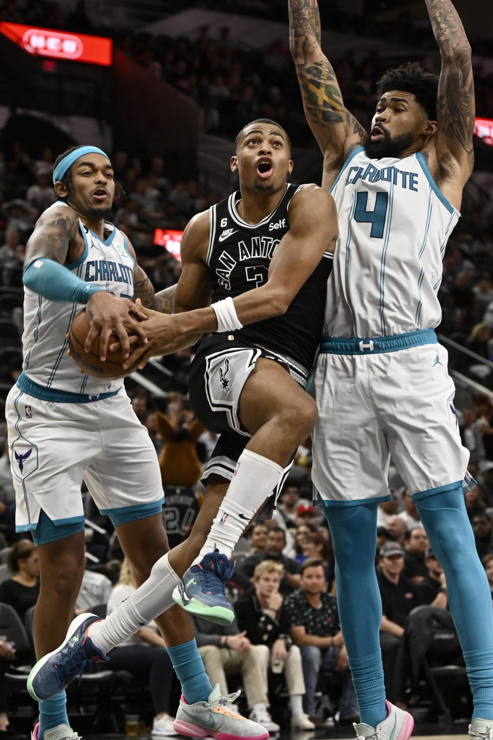 San Antonio Spurs' Keldon Johnson, center, drives to the basket against Charlotte Hornets' Nick Richards (4) and P.J. Washington during the second half of an NBA basketball game, Wednesday, Oct. 19, 2022, in San Antonio. Charlotte won 129-102. (AP Photo/Darren Abate)