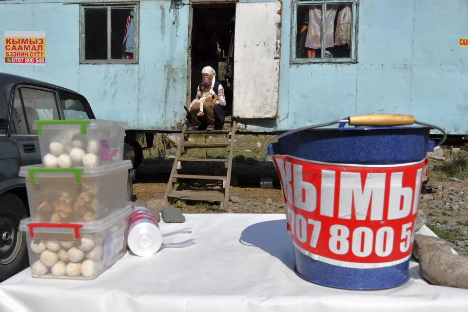 A Kyrgyz woman holds her baby as she sells kumis at a street market in Koy-Tash village, 30 kilometers (19 miles) south of the capital Bishkek, Kyrgyzstan, Saturday, Aug. 13, 2022. Kumis is a fermented milk drink popular in Central Asia that proponents say has health benefits. The grass and herbs lend flavor to the milk that locals draw from the mares in the fields where they graze. The milk then is left to ferment, or sometimes churned to promote fermentation, until it becomes mildly alcoholic.(AP Photo/Vladimir Voronin)