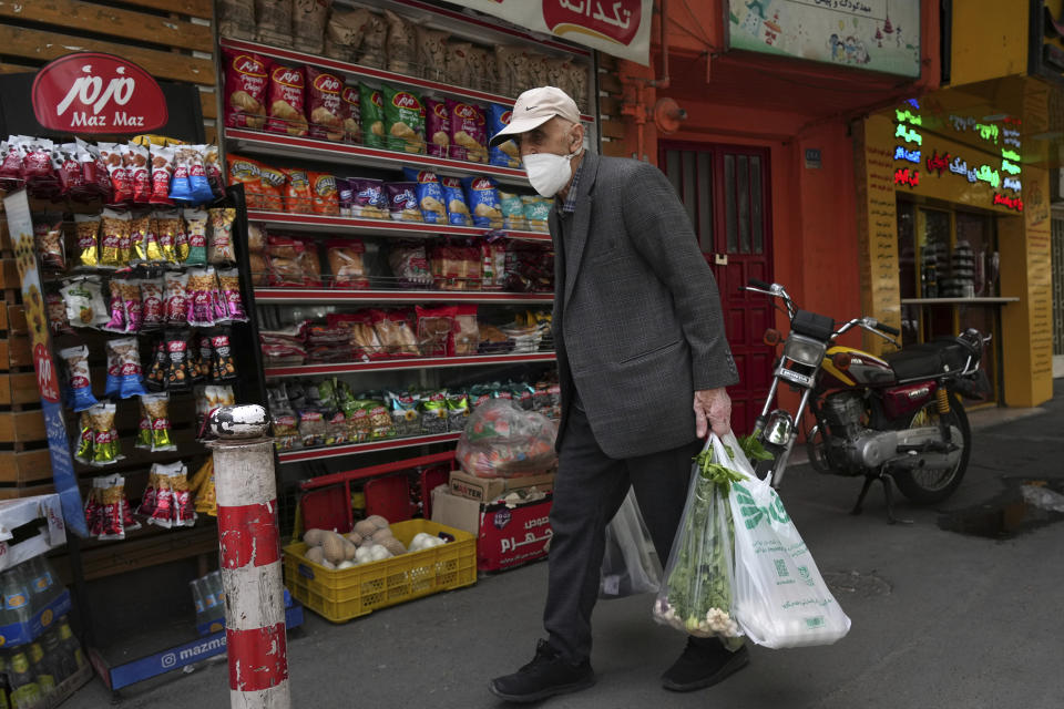 An elderly man carries his shopping in front of a grocery store in Tehran, Iran, Wednesday, May 11, 2022. Iran abruptly raised prices as much as 300% for a variety of staples such as cooking oil, chicken, eggs and milk on Thursday. (AP Photo/Vahid Salemi)