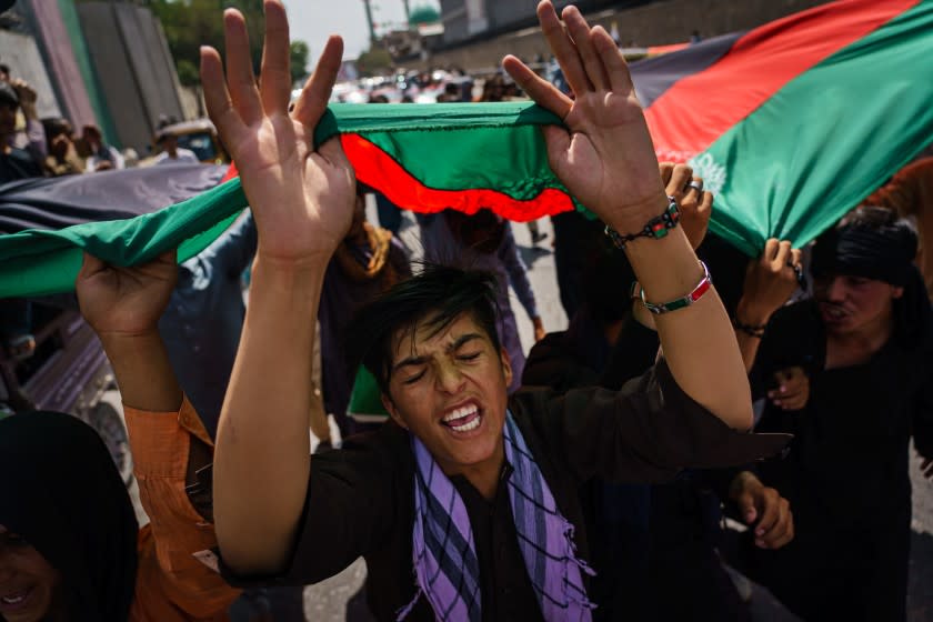 KABUL, AFGHANISTAN -- AUGUST 19, 2021: Afghans march down the street carrying banners and the flag of the Islamic Republic of Afghanistan, despite the presence of Taliban fighters around them, in Kabul, Afghanistan, Thursday, Aug. 19, 2021. About 200 people rallied towards the city center chanting ODeath to Pakistan, God Bless Afghanistan, Long Live the National Flag of Afghanistan.O \ (MARCUS YAM / LOS ANGELES TIMES)