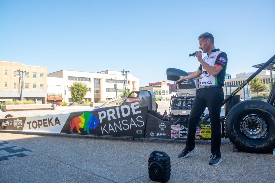 Travis Shumake shows off his drag racer at Evergy Plaza Wednesday morning detailing the number of world championships it has won. Shumake was recently sponsored by Visit Topeka and Pride Kansas as the first openly gay NHRA racer in history and will be competing this weekend at Heartland Park Speedway.