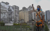 <p>En la imagen, el artista callejero y activista brasileño Mundano posa delante del mural que ha hecho en un edificio de la ciudad de Sao Paulo con cenizas que él mismo recogió de los incendios del Amazonas. (Foto: Miguel Schincariol / AFP / Getty Images).</p> 