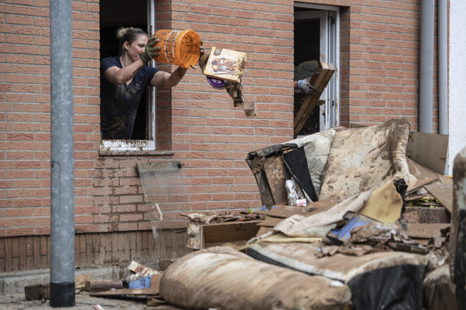 A woman throws rubbish from the window of her home onto a pile of discarded goods in the district of Blessem, in Ergfstadt, Germany, Thursday July 22, 2021. In the flood disaster area of Erftstadt-Blessem, some residents are being allowed back into their homes to clear debris after heavy rains caused devastating floods. (Marius Becker/dpa via AP)