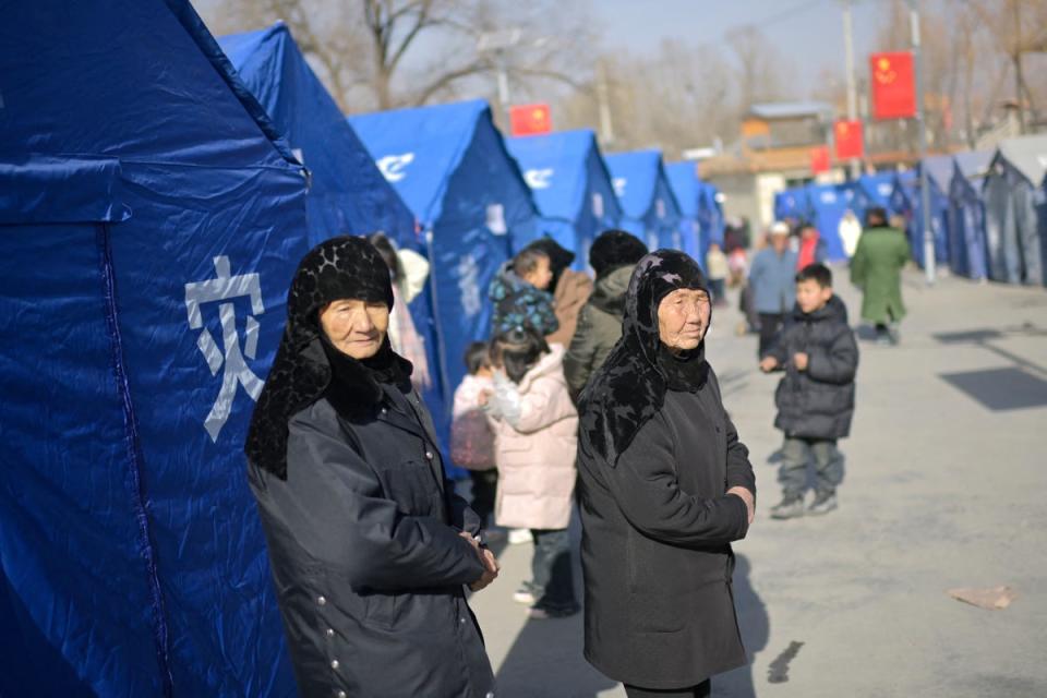 Earthquake-affected residents look on beside aid tents erected in a school compound in the village of Gaoli, in Jishishan (Getty)