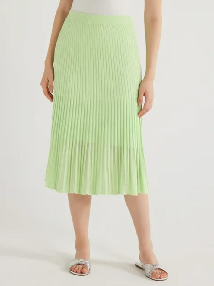 Person in a pleated midi skirt and slide sandals, standing