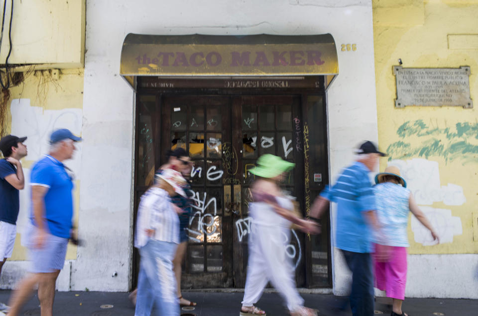 Tourists walk past a closed taco restaurant the day after anti-government protests broke out in San Juan, Puerto Rico, Thursday, July 18, 2019. Protesters are demanding Gov. Ricardo Rossello resign after the leak of online chats that show him making misogynistic slurs and mocking his constituents. (AP Photo/Dennis M. Rivera Pichardo)