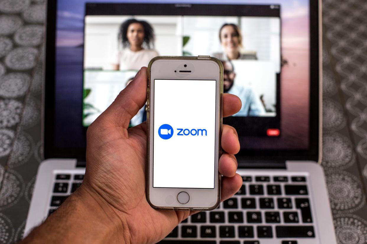 Zoom app seen displayed on a smartphone screen and a Zoom Desktop on a laptop in the background.