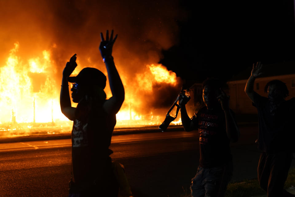 FILE - In this Aug. 24, 2020, file photo, protesters walk past police with their arms up, in Kenosha, Wis., as a building burns in the background. The federal government deliberately targeted Black Lives Matter protesters via heavy-handed criminal prosecutions in an attempt to disrupt and discourage the global movement that swept the nation last summer in the wake of the police killing of George Floyd, according to a new report released Wednesday, Aug. 18, 2021, by The Movement for Black Lives. (AP Photo/David Goldman, File)