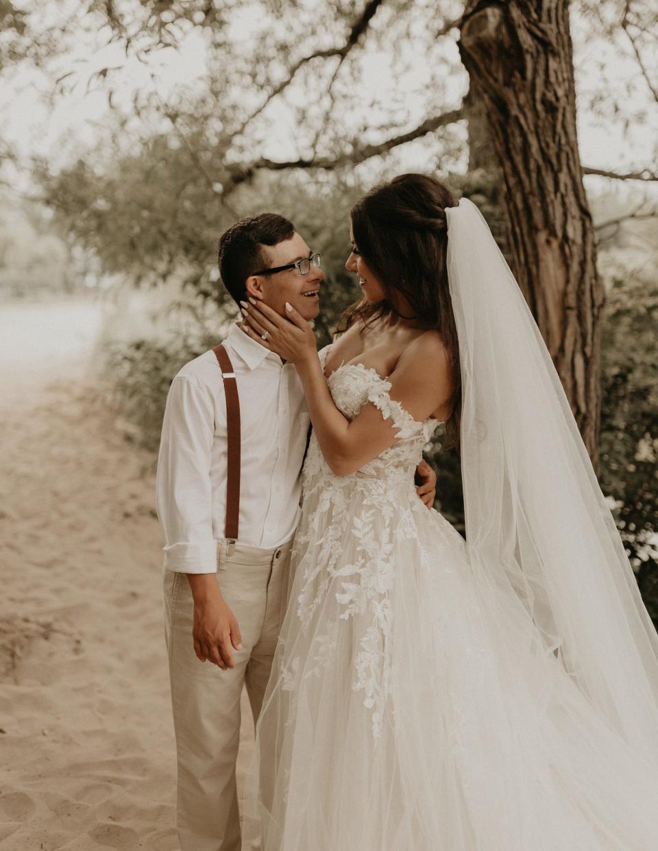 A bride touches her brother's face on a beach.