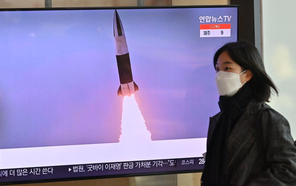 A woman walks past a television screen showing a news broadcast with file footage of a North Korean missile test, at a railway station in Seoul on January 20, 2022, after North Korea hinted it could resume nuclear and long-range weapons tests, as it prepared for 