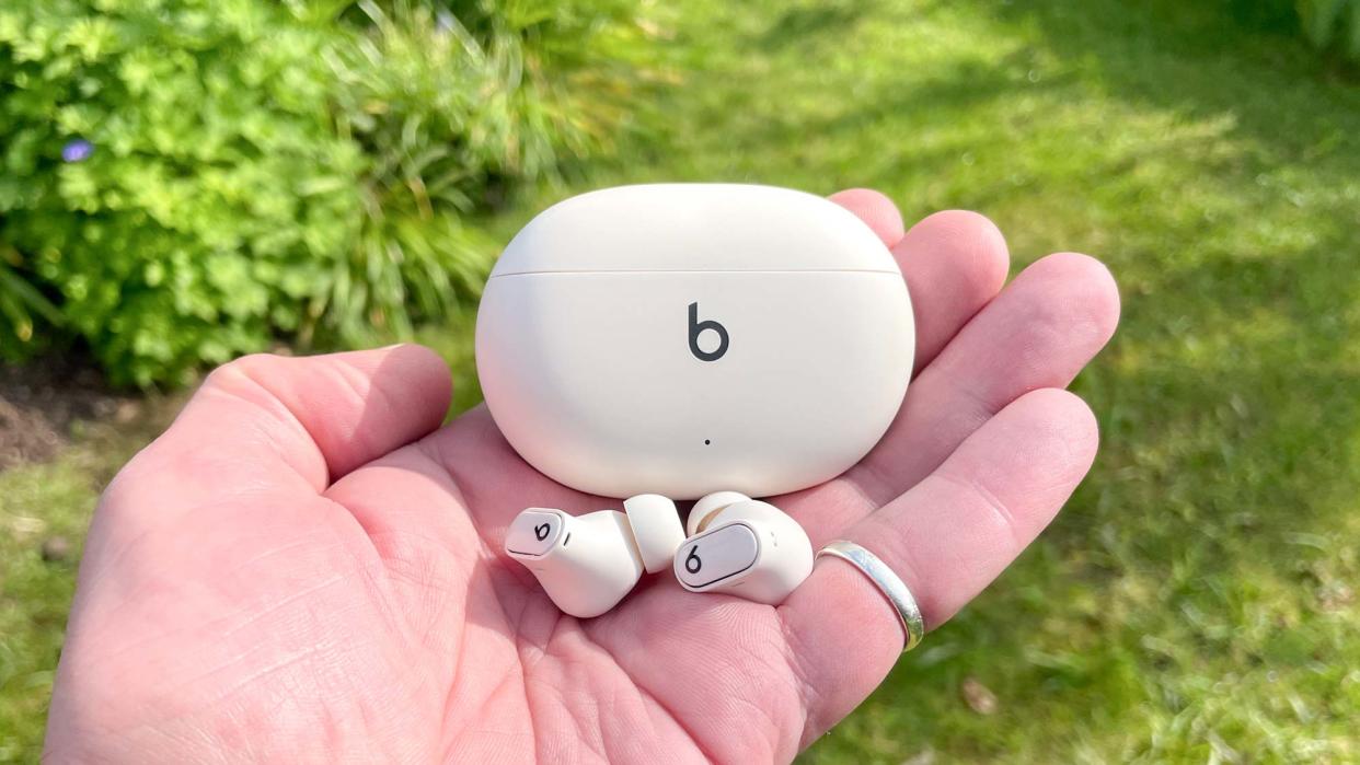  Beats Studio Buds+ in ivory held in hand with charging case. 