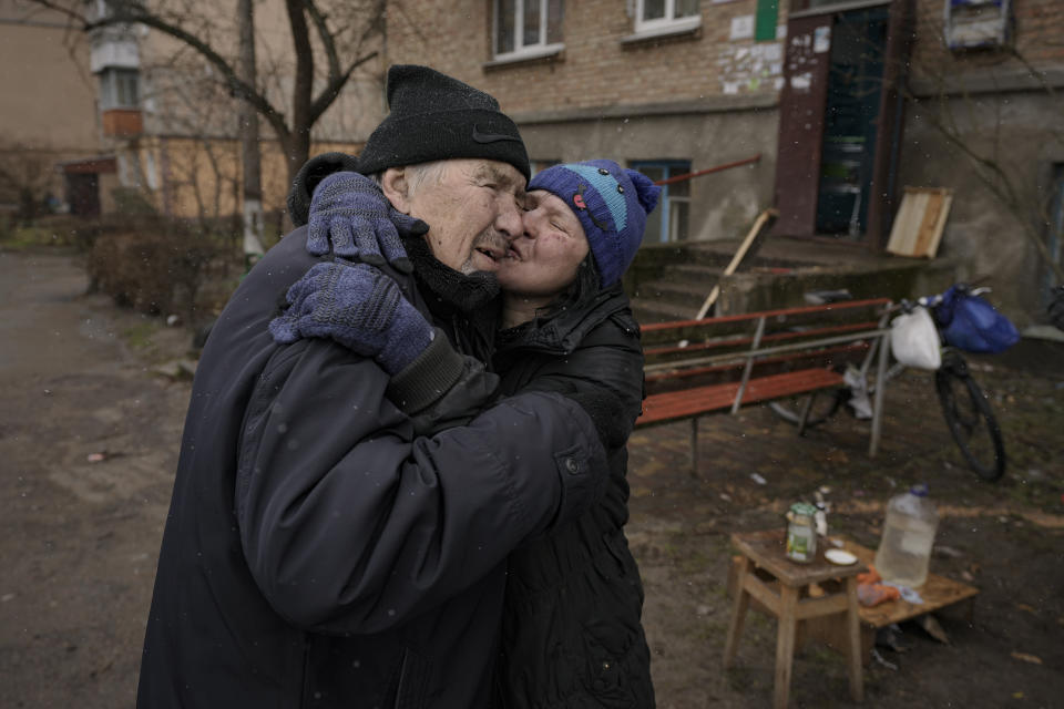 A woman kisses a man while cooking on an open fire outside an apartment building which had no electricity, water or gas since the beginning of the Russian invasion in Bucha, Ukraine, Sunday, April 3, 2022. (AP Photo/Vadim Ghirda)