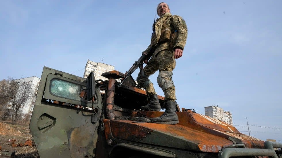 A Ukrainian soldier stands atop a destroyed Russian APC after recent battle in Kharkiv, Ukraine, Saturday, March 26, 2022.