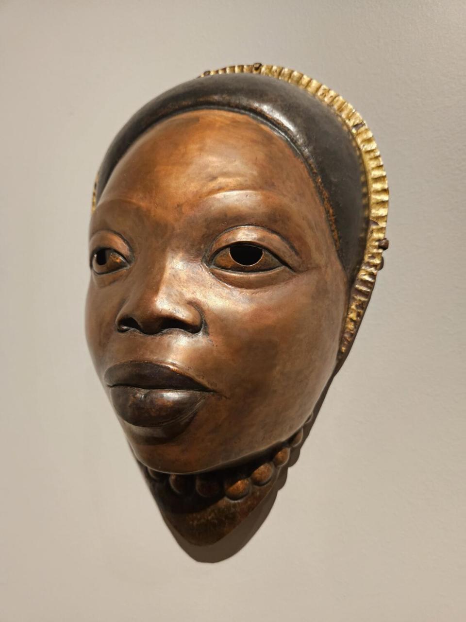 A copper mask of Black mother with a gold headband.