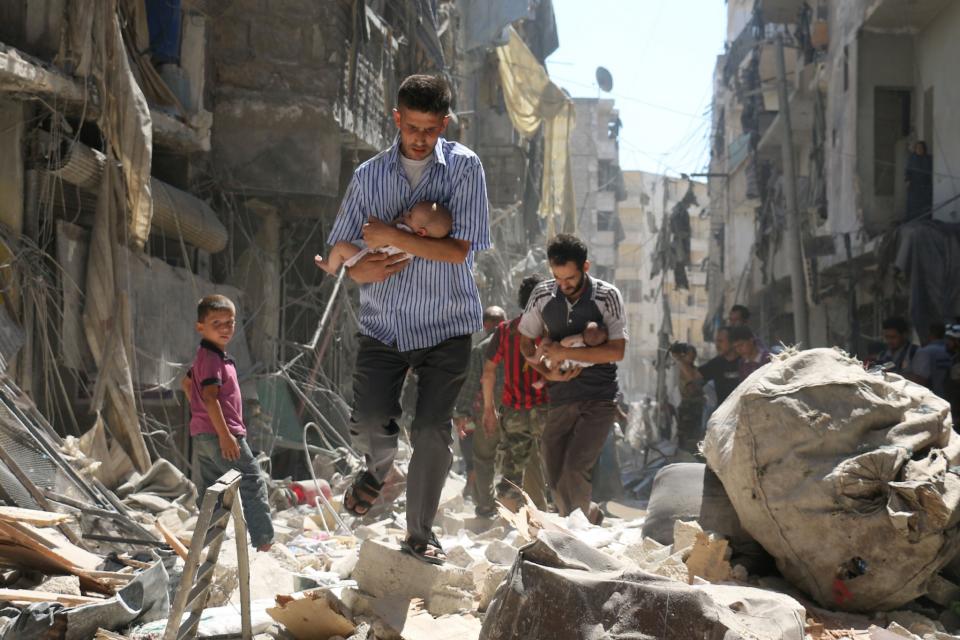 Syrian men carrying babies make their way through the rubble of destroyed buildings following a reported air strike on the rebel-held Salihin neighbourhood of the northern city of Aleppo, on September 11, 2016. (Photo: Ameer AlhalbiI/AFP/Getty Images)