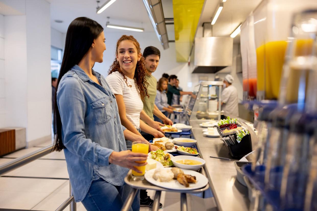 Happy high school kids eating at a buffet style cafeteria and holding their trays