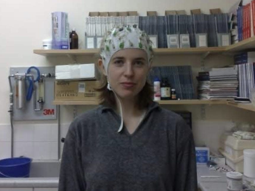 Liza Bec is shown in a clinical lab wearing a helmet covered in electrodes.