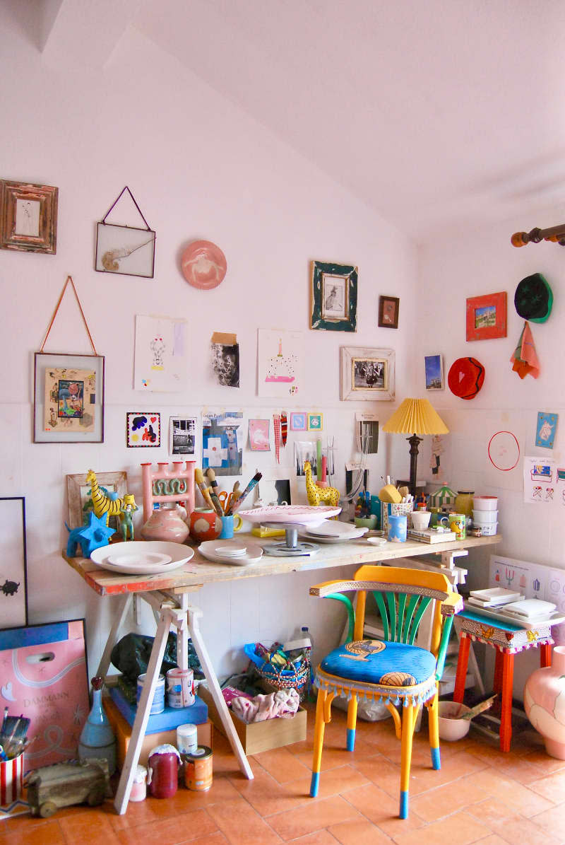 Art supplies on desk in white room with gallery walls.