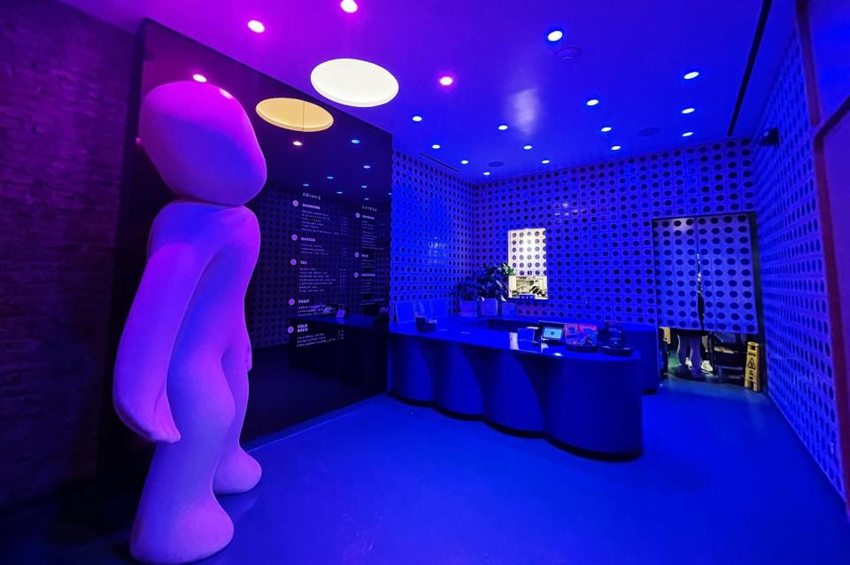 A large white, featureless statue stands in left corner of the interior of blue-hued Jellyman Tea, near the register.