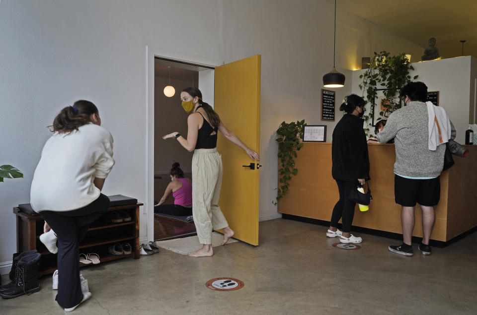 Yoga instructor Lydia Stone, center, welcomes patrons arriving for a morning yoga class at the Highland Park Yoga studio in Los Angeles, Saturday, Nov. 6, 2021. A vaccine mandate that is among the strictest in the country takes effect Monday, Nov. 8, in Los Angeles, requiring proof of shots for everyone entering a wide variety of businesses from restaurants to shopping malls and theaters to nail and hair salons. (AP Photo/Damian Dovarganes)