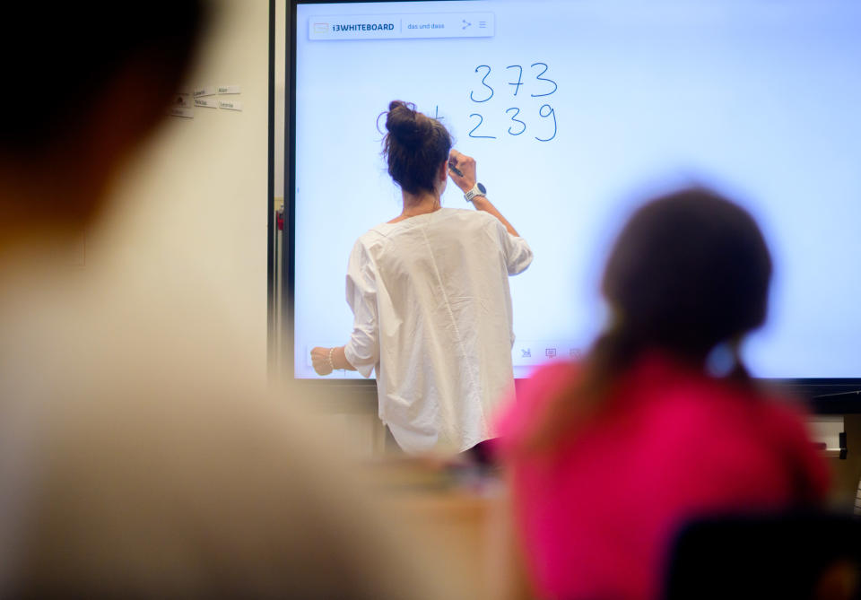 Eine Lehrerin schreibt eine Mathematikaufgabe auf eine digitale Schultafel im Klassenraum einer 4. Klasse einer Grundschule (Bild: dpa) 