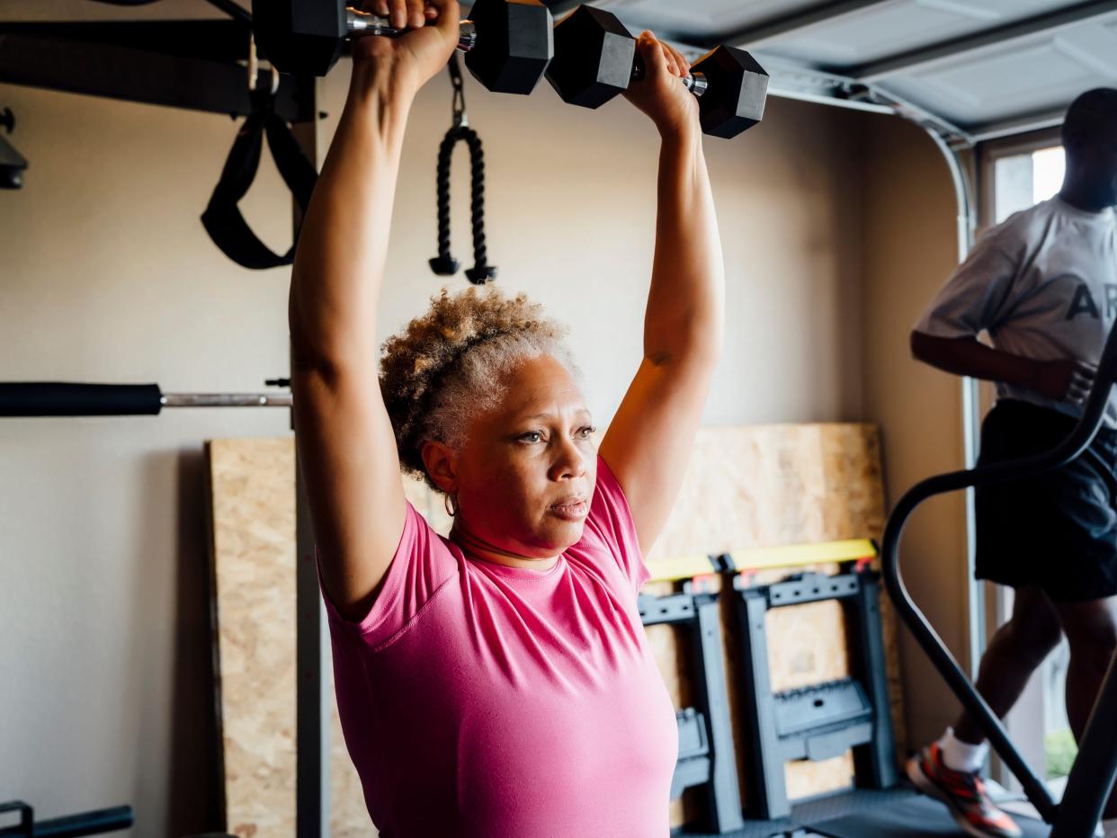 A woman lifting weights while a man is on a treadmill.