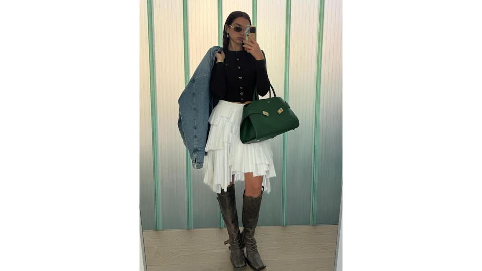 Dua Lipa poses for a mirror selfie in a white skirt, knee-high boots and knitted cardigan before heading off to work