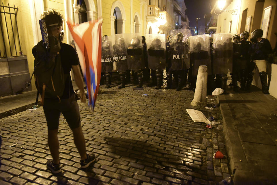 A demonstrator with a Puerto Rican flag stands in front of the police during clashes in San Juan, Puerto Rico, Wednesday, July 17, 2019. Thousands of people marched to the governor's residence in San Juan on Wednesday chanting demands for Gov. Ricardo Rossello to resign after the leak of online chats that show him making misogynistic slurs and mocking his constituents. (AP Photo /Carlos Giusti)