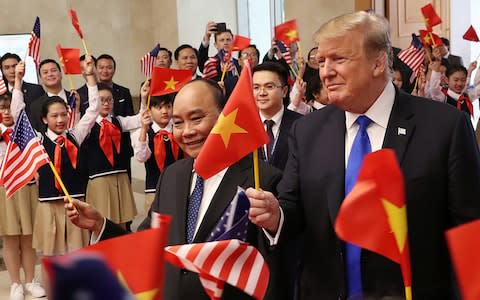 Donald Trump and Vietnamese Prime Minister Nguyen Xuan Phuc hold flags as they are greeted by students  - Credit: LEAH MILLIS/REUTERS