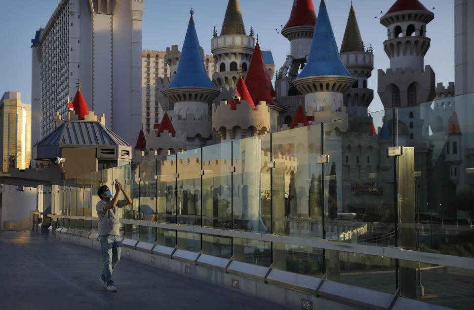 In this April 18, 2020, photo, a man wearing a mask as a precaution against the coronavirus takes pictures along the Las Vegas Strip in Las Vegas. (AP Photo/John Locher)