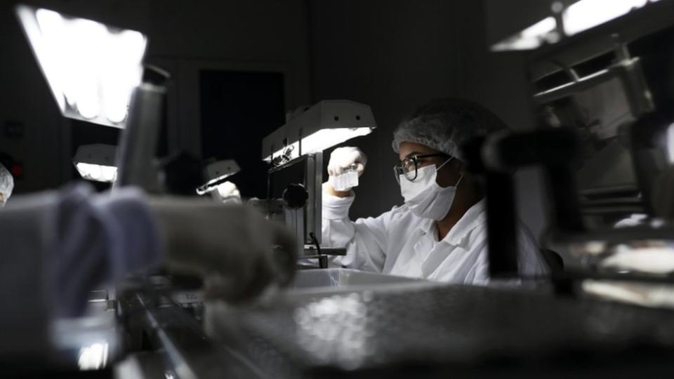 Un investigador con mascarilla observando frascos de dosis de fármacos.