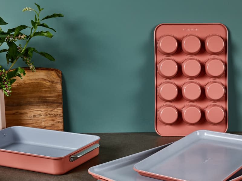 Caraway Home bakeware (muffin pan, cake pans, bread pans) in perracotta color on counter with green wall behind