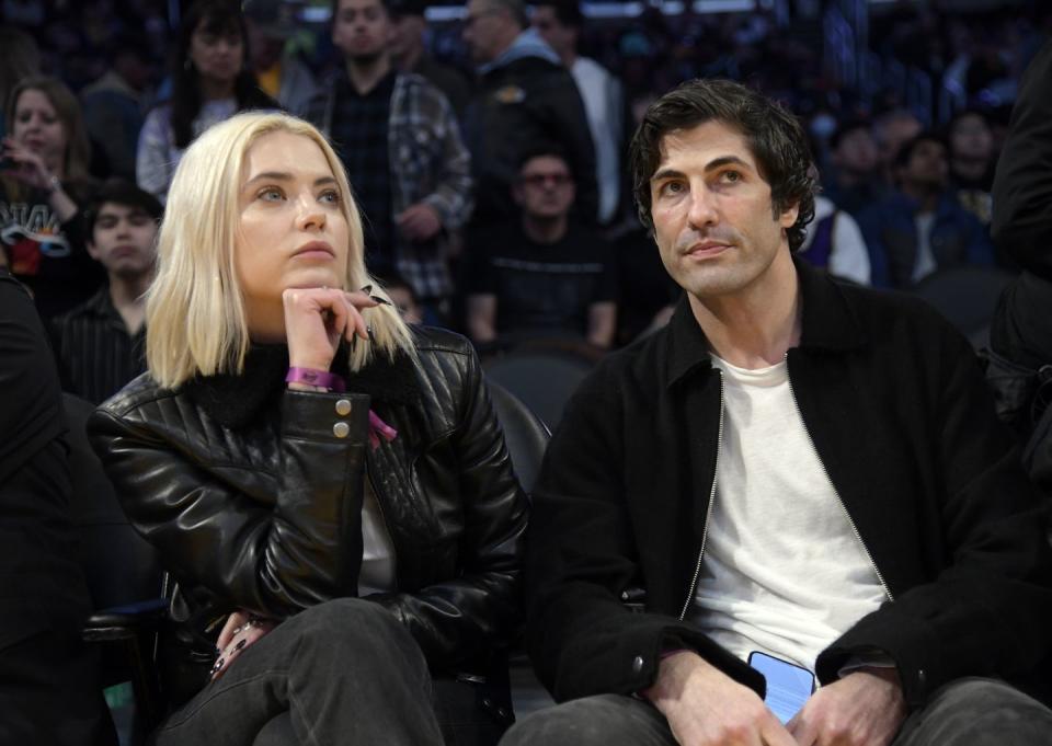 ashley benson and brandon davis sat watching a sports game, both dressed in mostly black, ashley has her hand on her chin