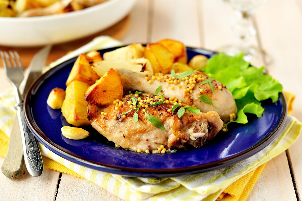 Baked honey mustard chicken with a side of potatoes on a dark blue plate with a fork and knife on yellow napkins on a wooden table with a blurred background