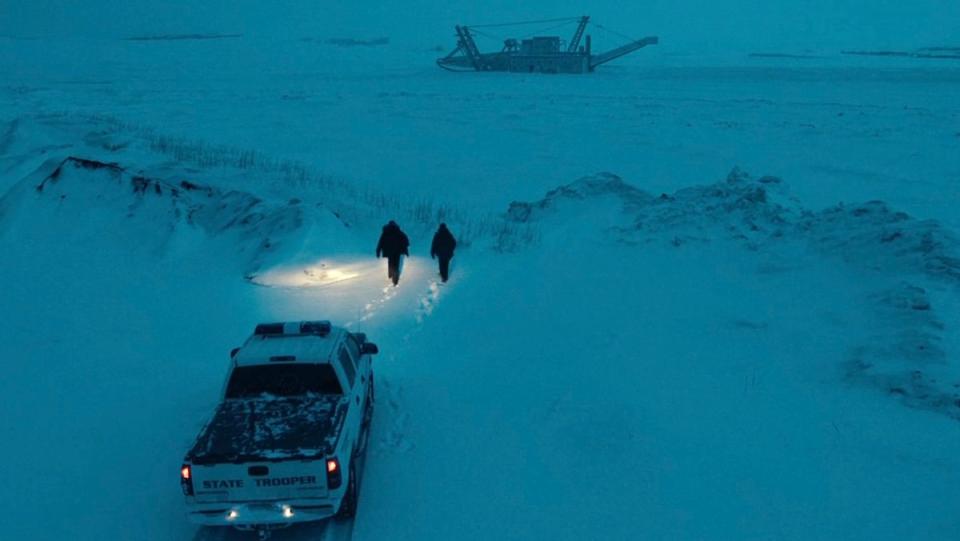 Danvers and Navarro walking from their truck with its lights on to a frozen water with a barge in True Detective: Night Country