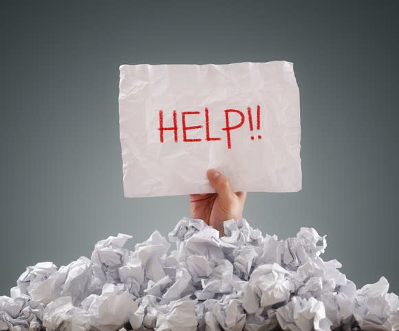 Person buried under a pile of bills holding help sign