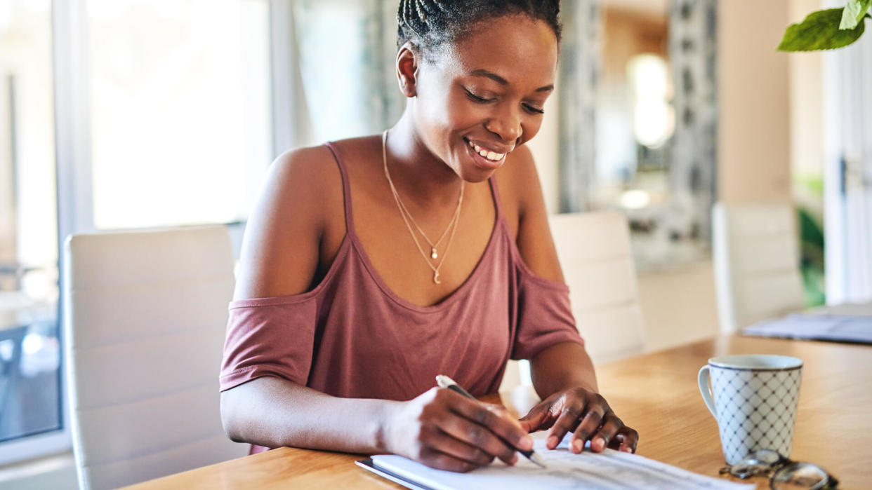 Cropped shot of a young woman filling out paperwork at home.