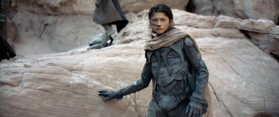 Zendaya standing next to a rock formation in a scene from Dune