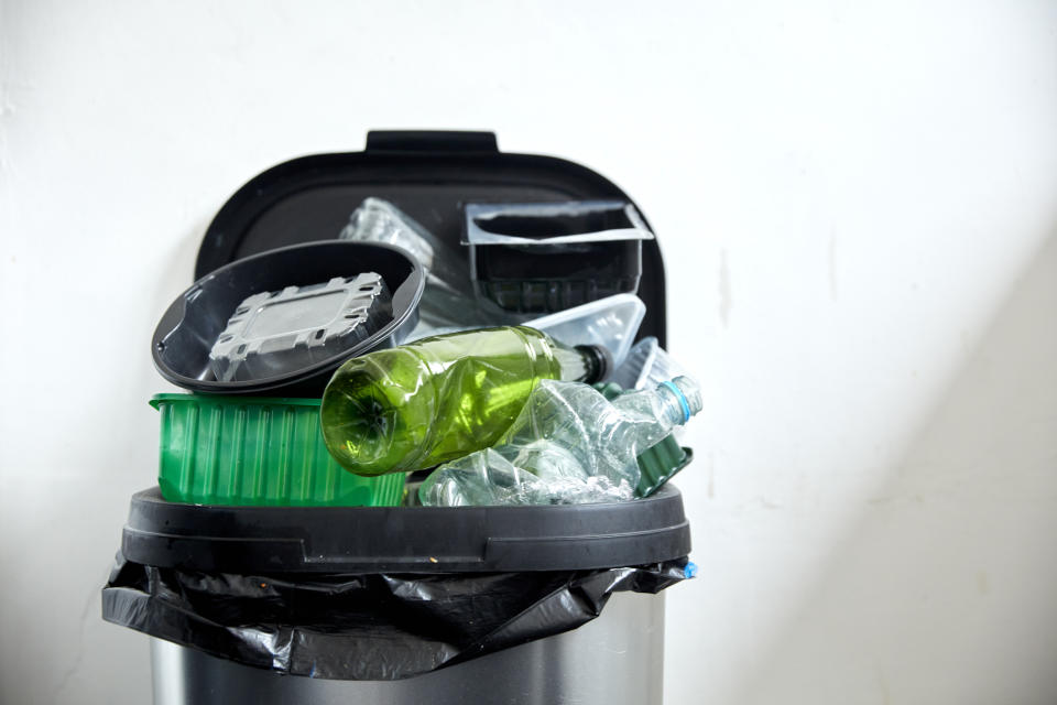 An overflowing trash bin with plastic bottles and food packaging